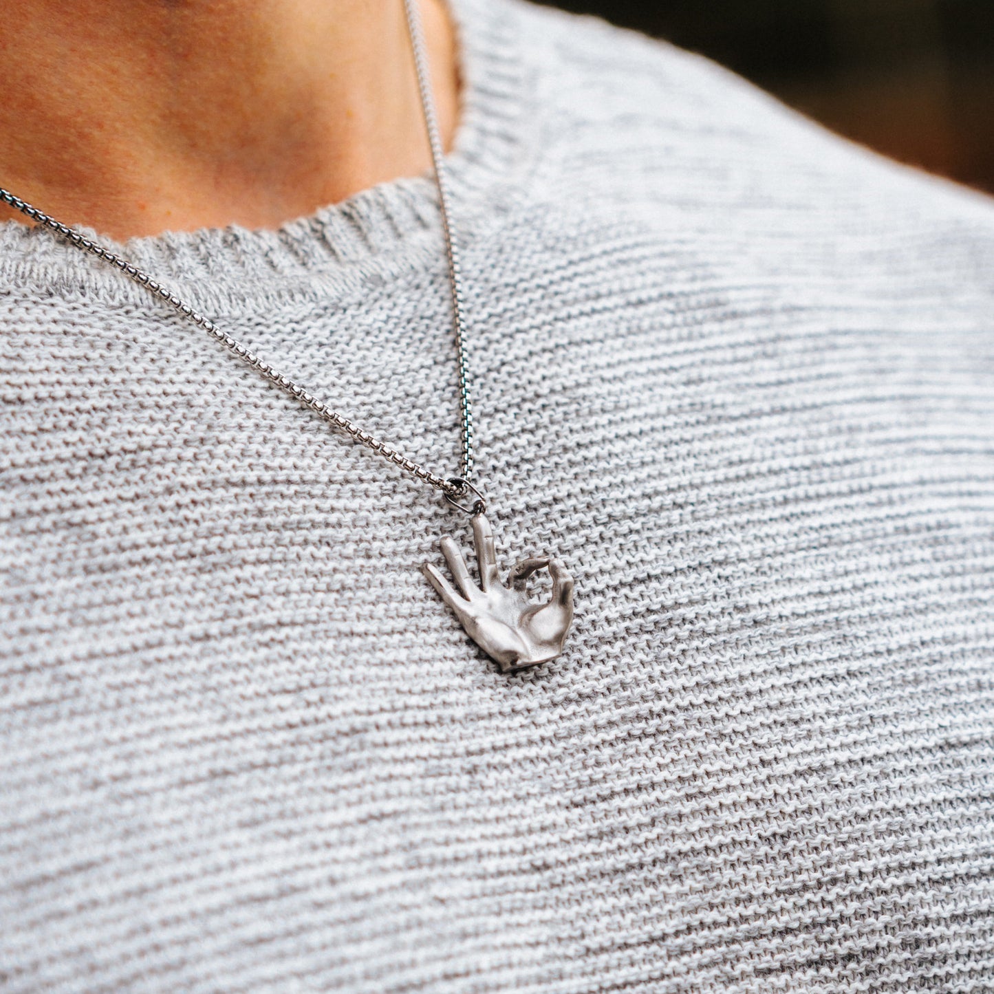 Necklace with a hand-shaped pendant on a person wearing a gray sweater.