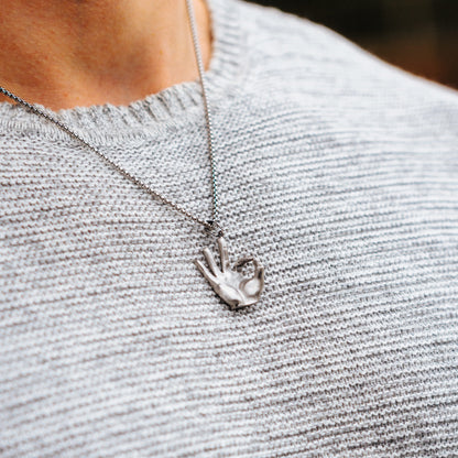 Necklace with a hand-shaped pendant on a person wearing a gray sweater.