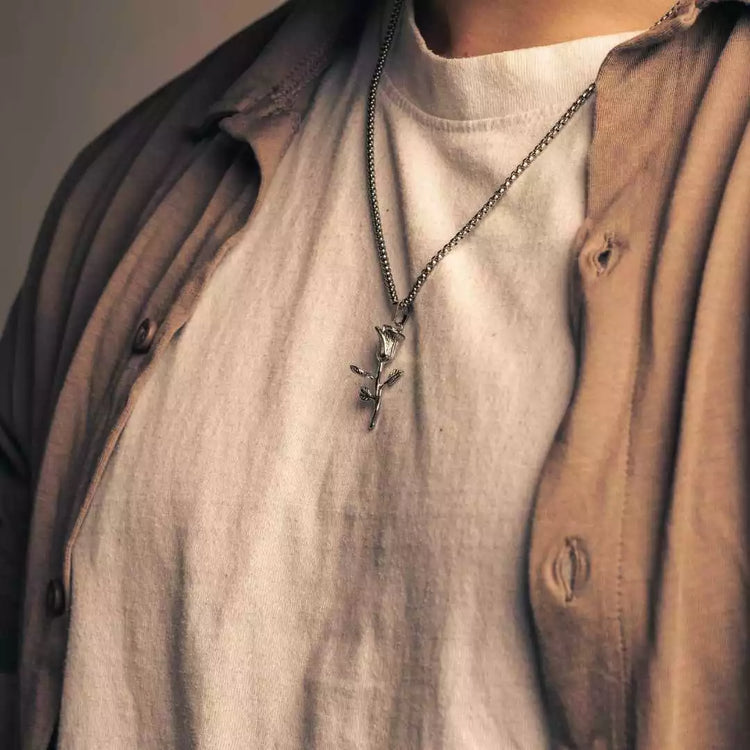 Person wearing a rose necklace with a pendant, dressed in layered clothing.